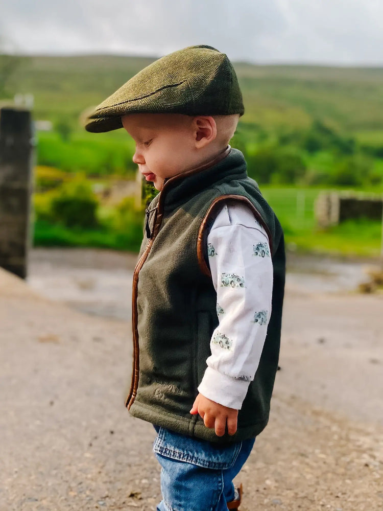 Child wearing a green flat cap, fleece gilet, and jeans with a land rover top